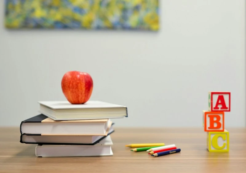 A desk with a stack of books, an apple, colored pencils and alphabet blocks