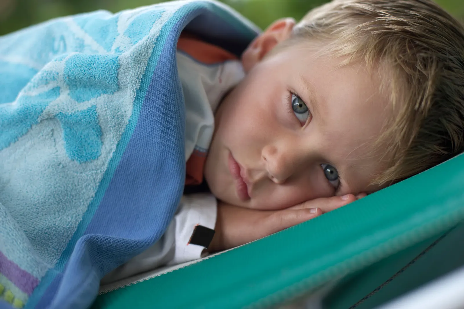 A tired young boy rests his head on his hands, wrapped in a soft blue towel