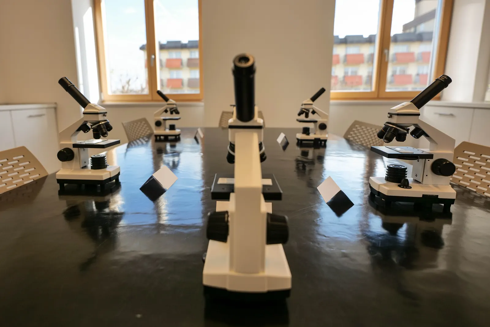 A lab table set with six student microscopes in a bright classroom