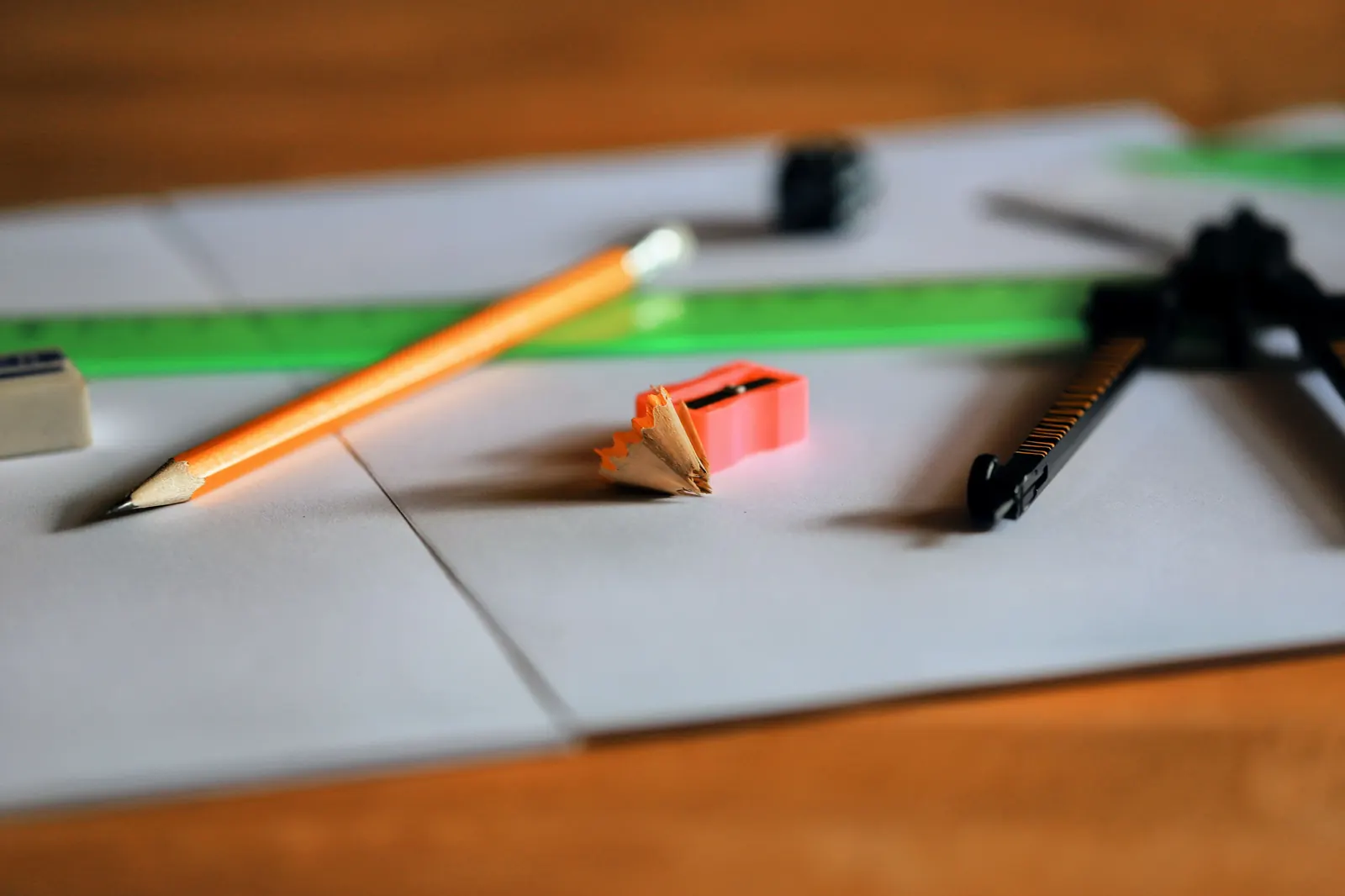 A sharpened pencil, a pencil sharpener with shavings and a drawing compass on white paper