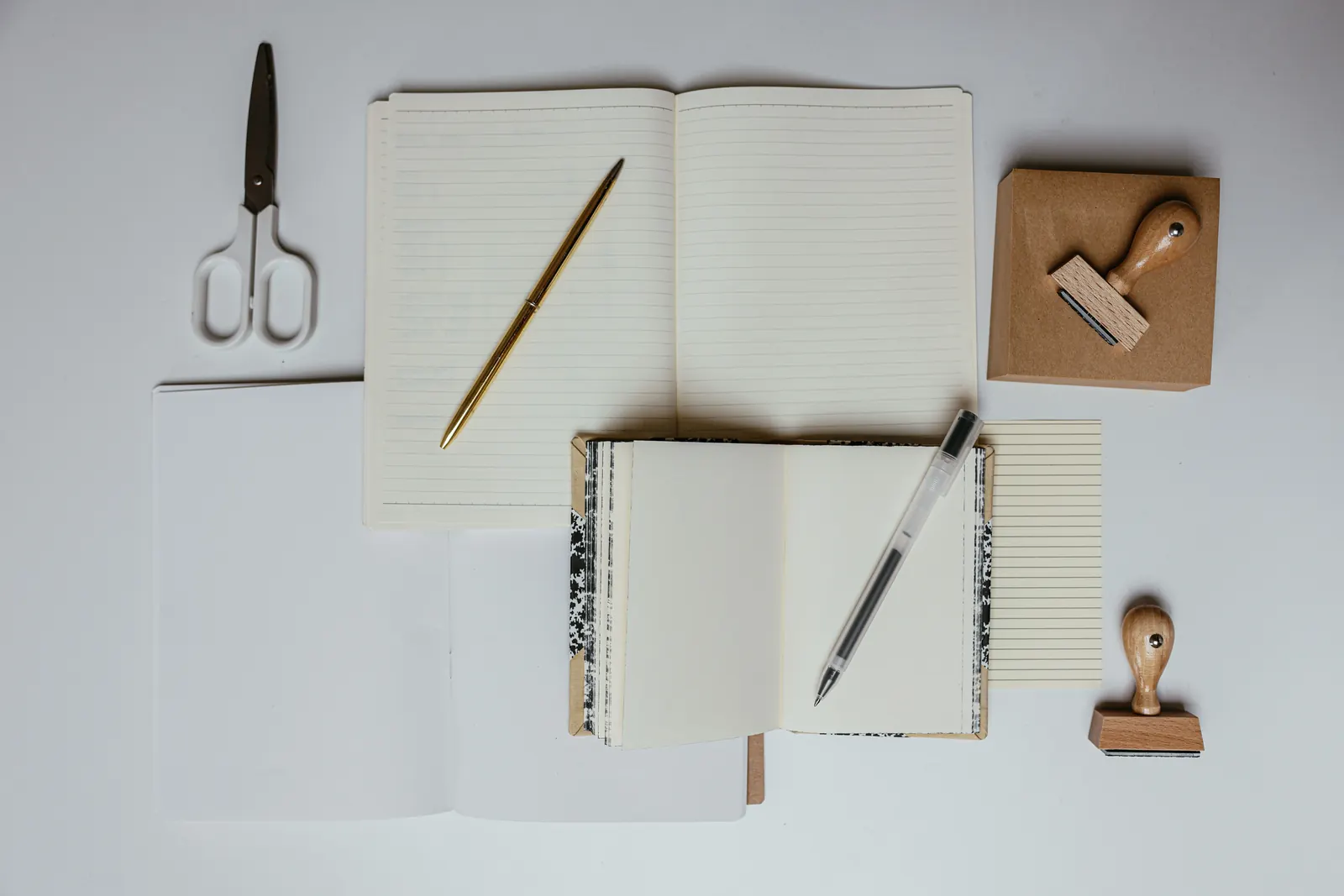 Open notebooks, scissors, a pen and a wooden rubber stamp laid out on a pale grey desk