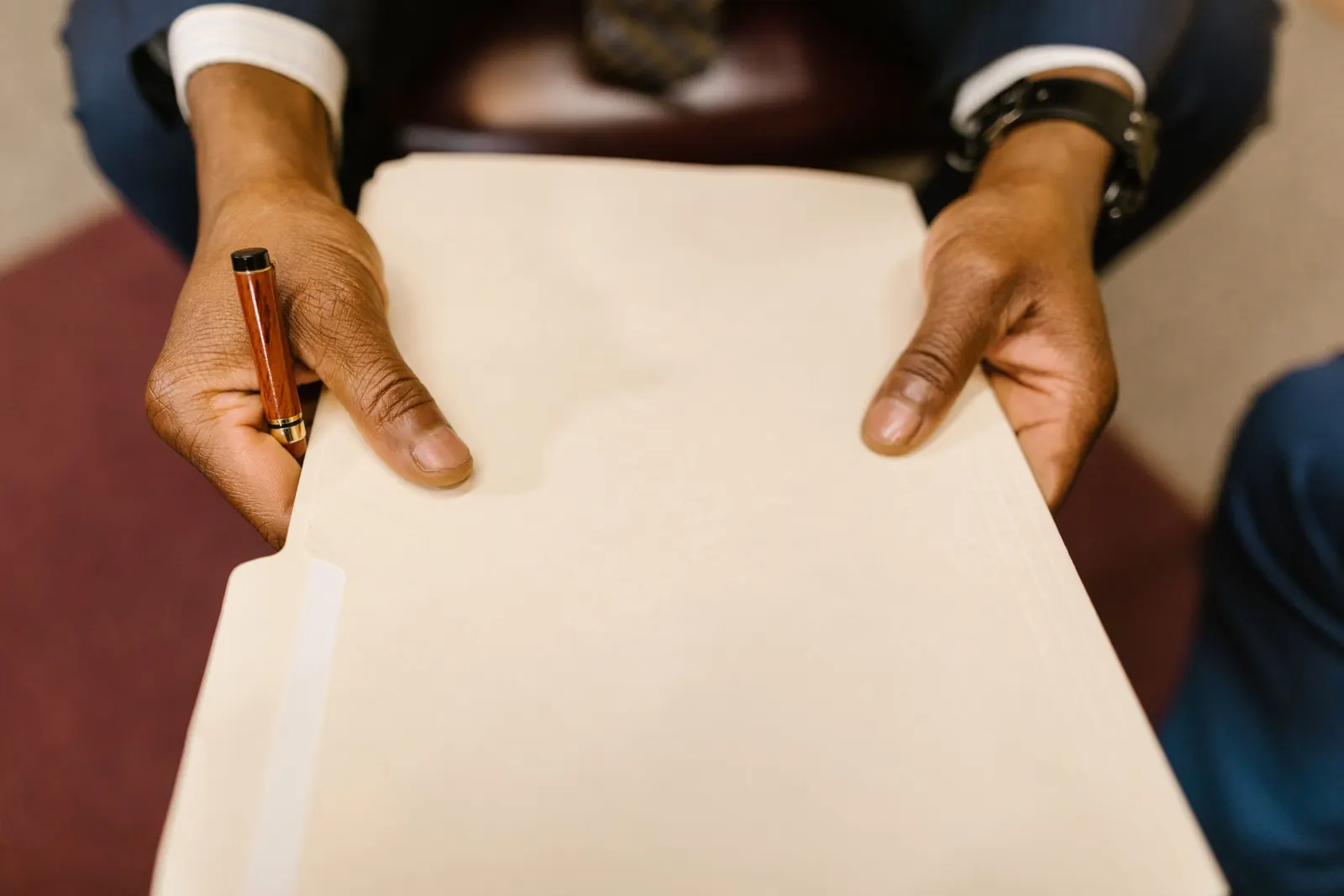 A man's hands hold out a blank manila folder, a wooden pen between his fingers