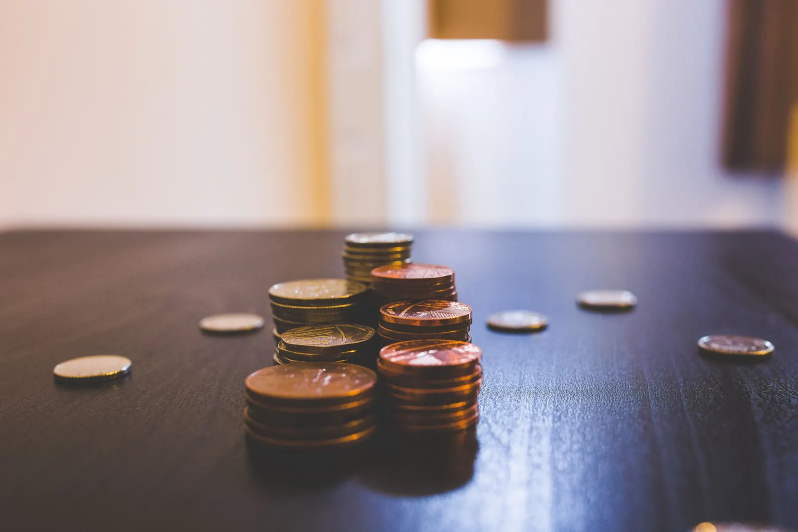 Small stacks of copper and gold coins on a dark wooden table in window light