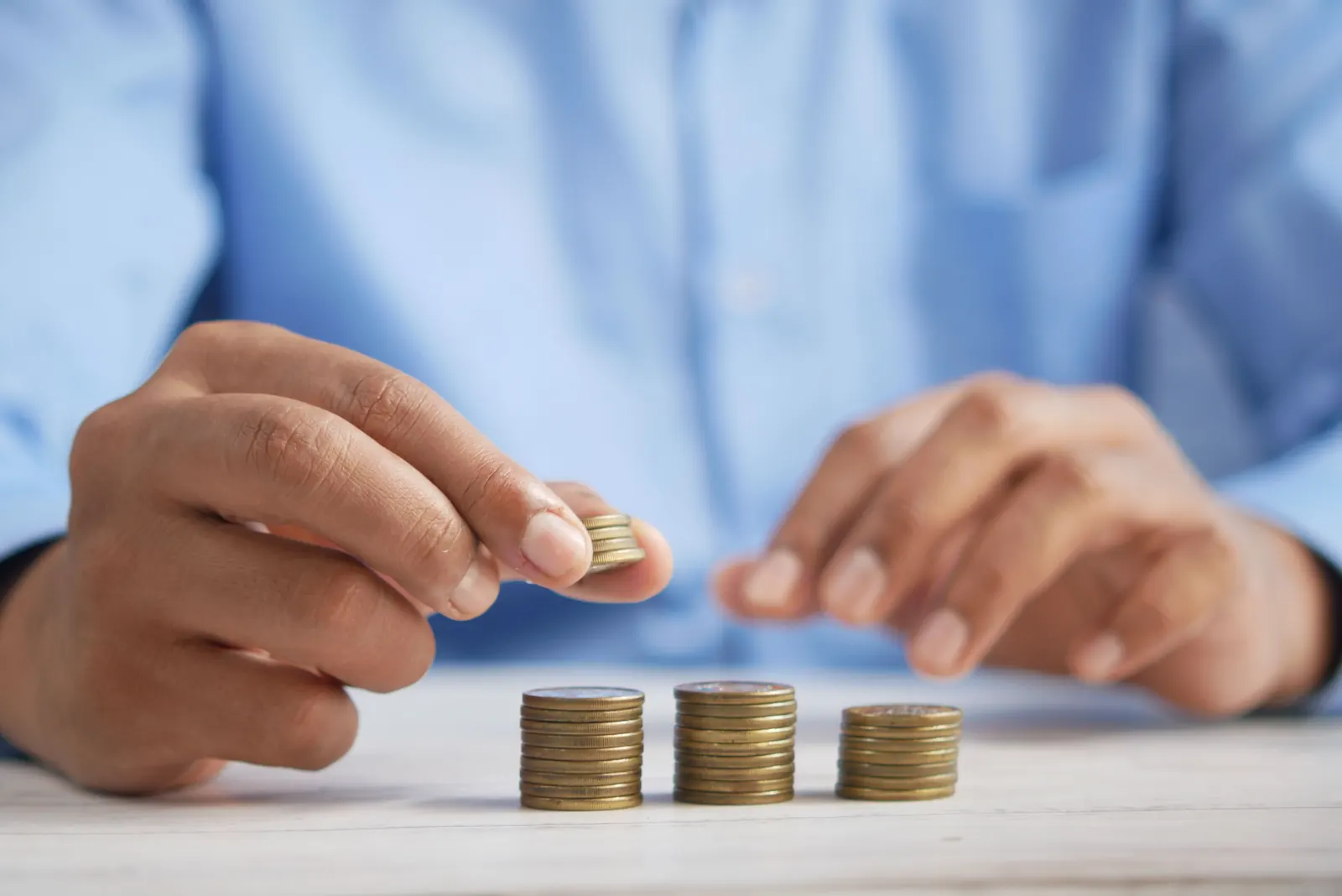 A man's hands build three small stacks of coins on a white table