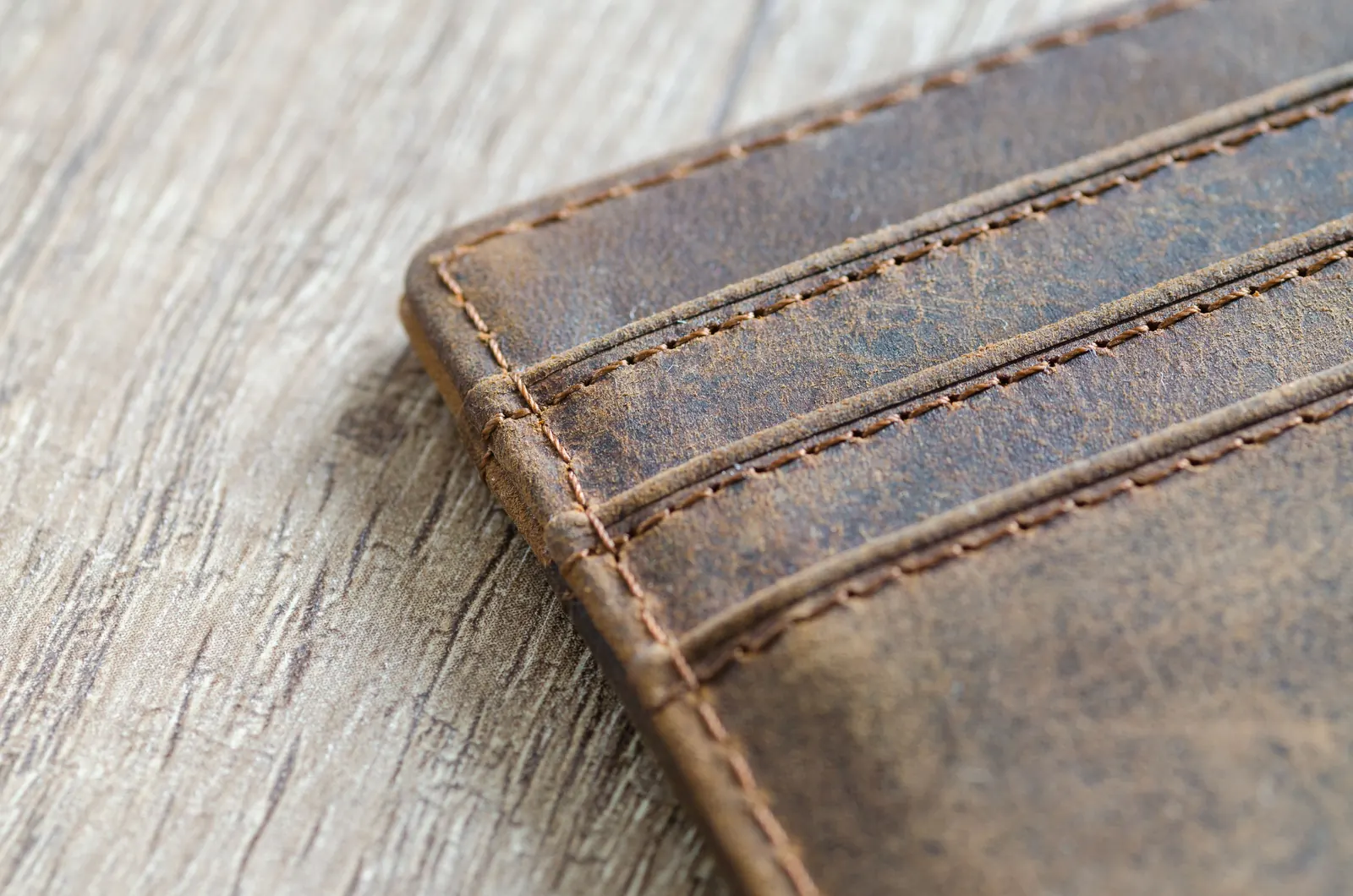 A worn brown leather wallet with stitched card slots on a pale wooden table