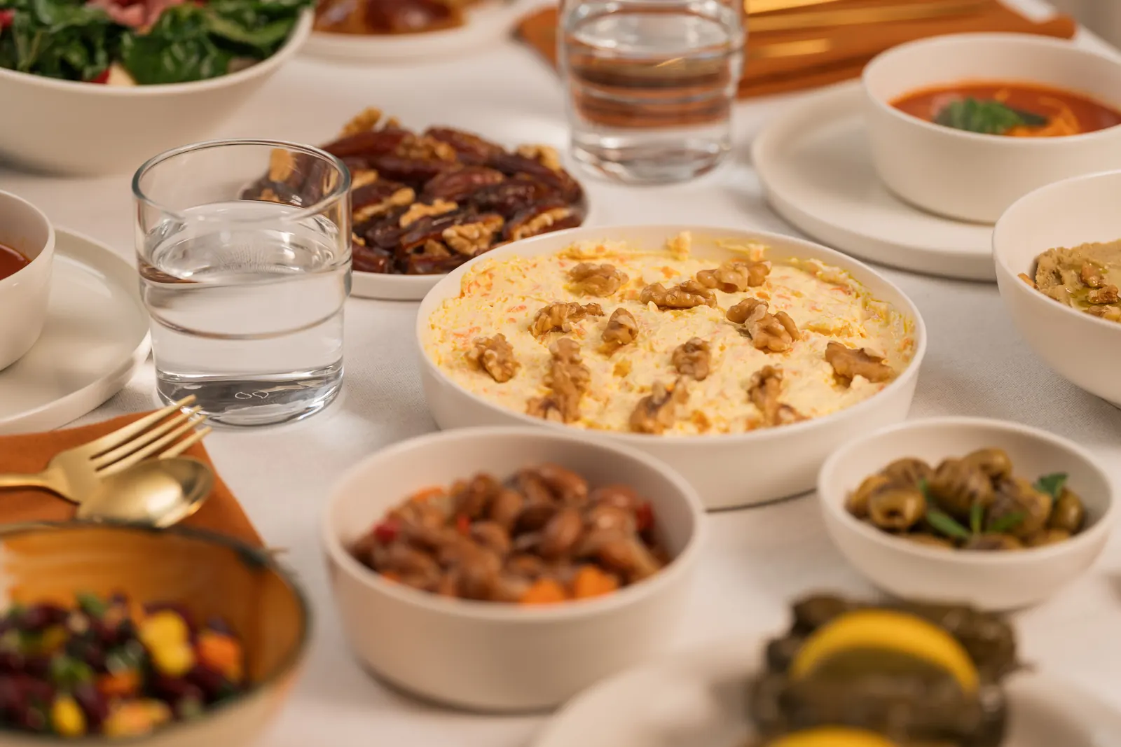 A table laid with bowls of salad, soup, dates, olives and a walnut-topped dish beside glasses of water
