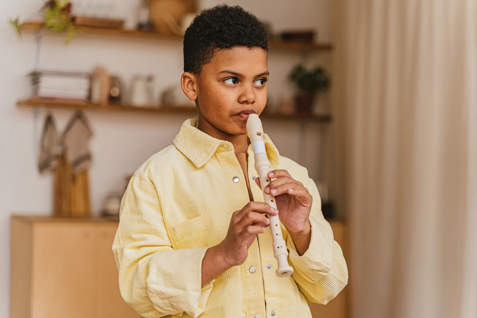 A boy in a yellow shirt plays a recorder in a warm, wood-shelved room