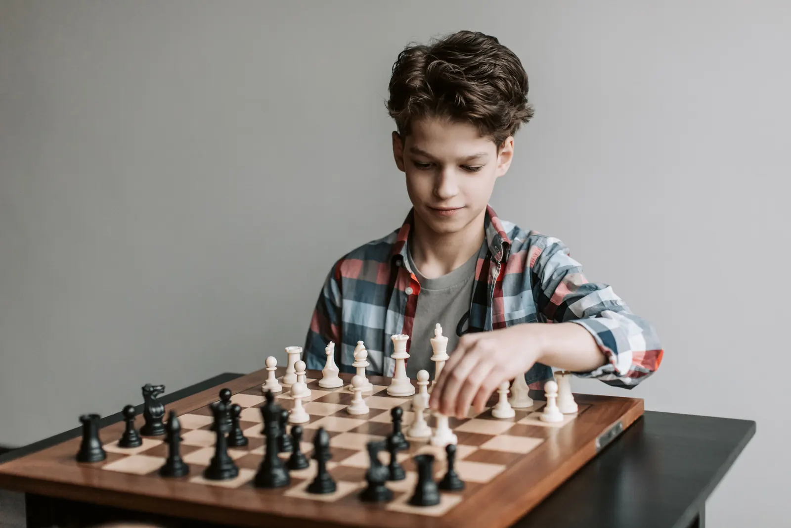 A boy in a plaid shirt moves a piece on a wooden chessboard