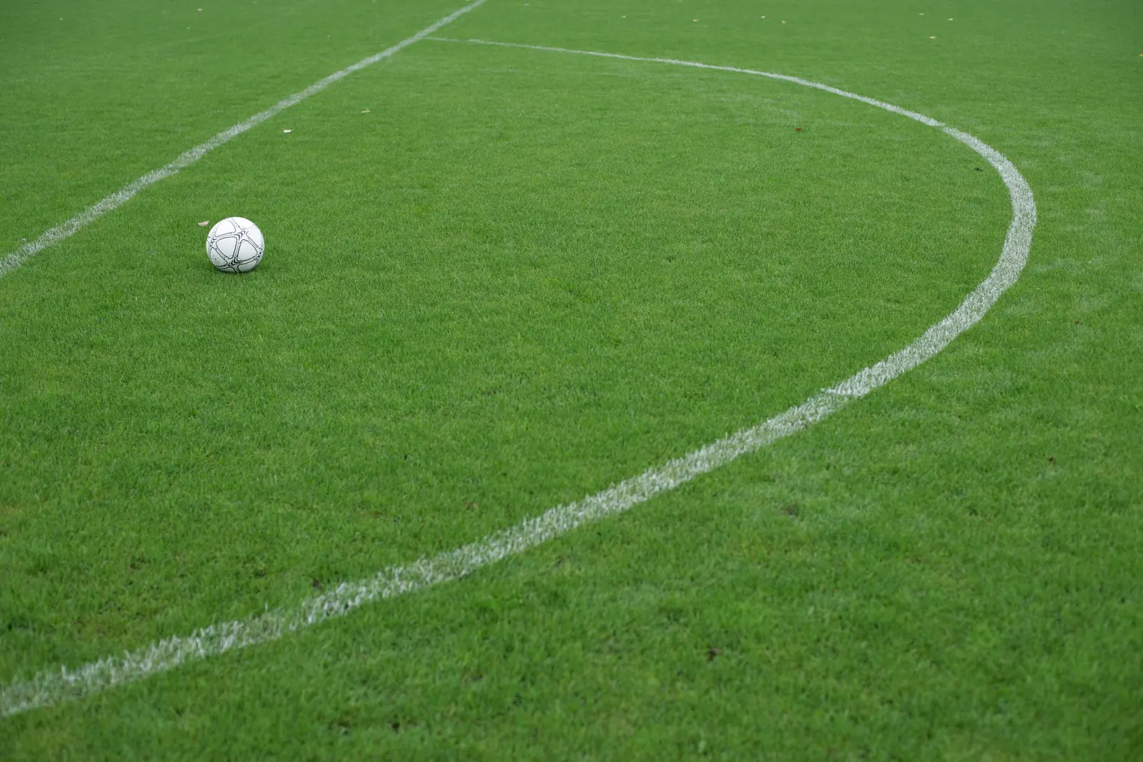 A white football resting on the grass of an empty pitch beside the curve of the centre circle