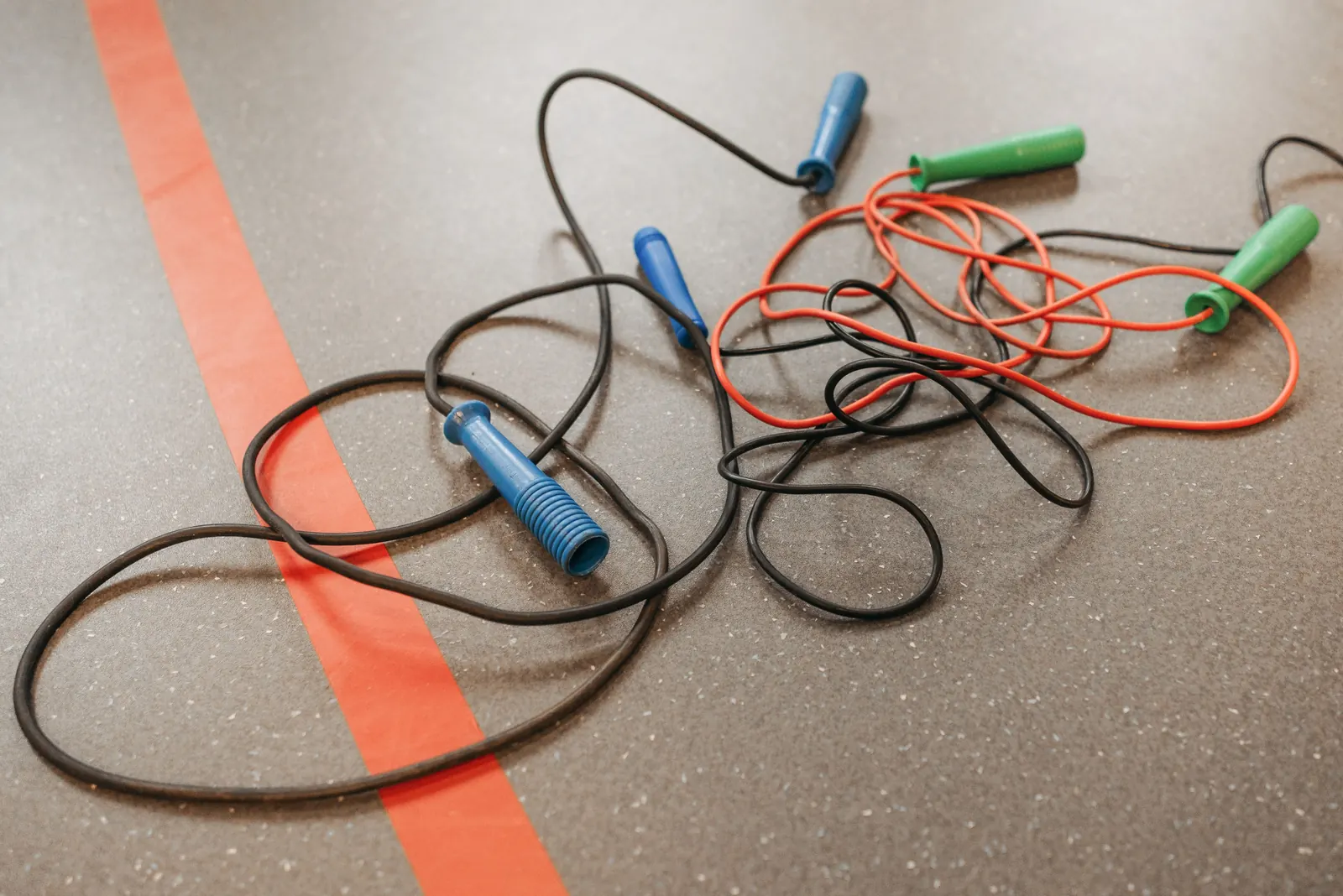 Skipping ropes with blue and green handles lie tangled on a speckled gym floor beside a painted court line