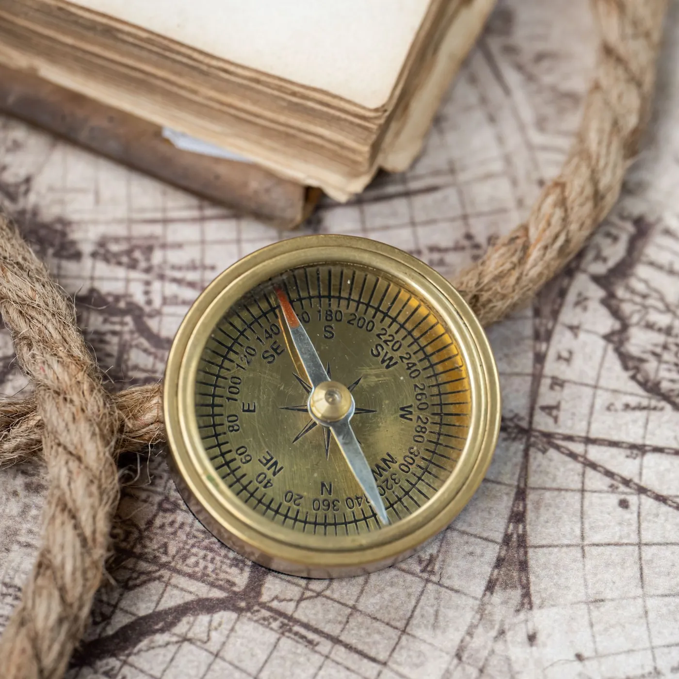 A brass compass on an antique-style world map, looped with coiled rope, beside the corner of an old closed book