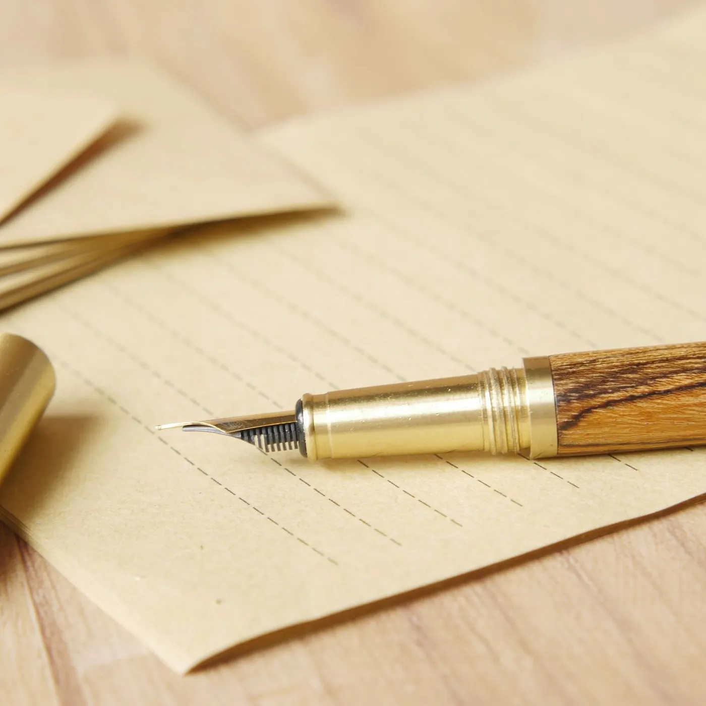 A wood-and-brass fountain pen with its cap off, lying on lined kraft paper beside a stack of envelopes