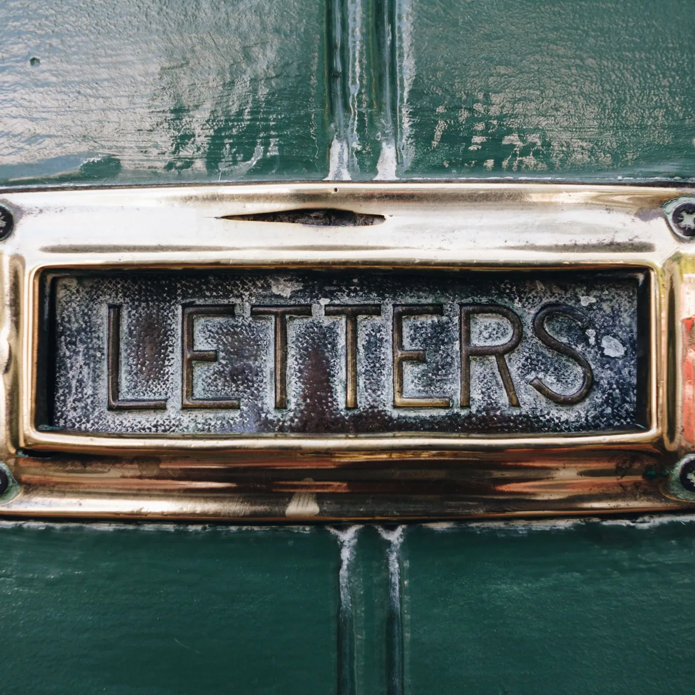 A polished brass letterbox marked LETTERS set into a glossy dark green front door