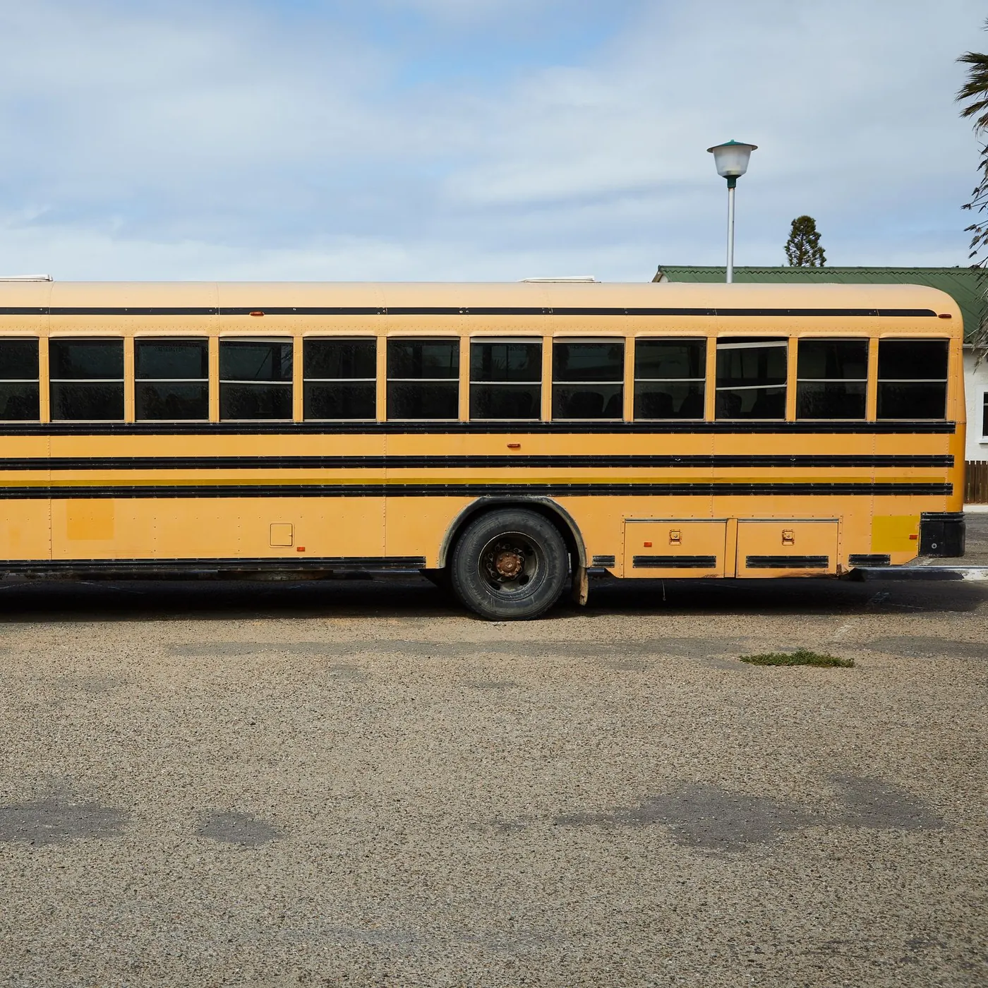 A long yellow school bus parked side-on in an empty lot under a pale blue sky with light clouds
