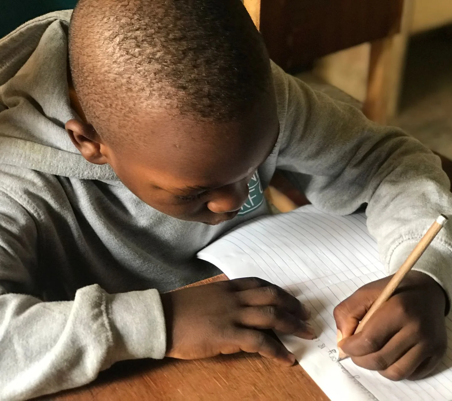 A school-age boy writing carefully in a notebook
